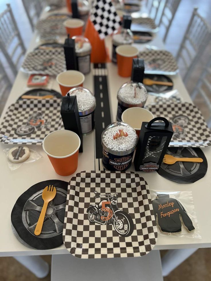 a long table with black and white checkered plates, silverware and cups on it