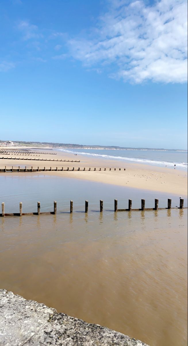 there is a long wooden pier in the water at the edge of the beach with people walking on it