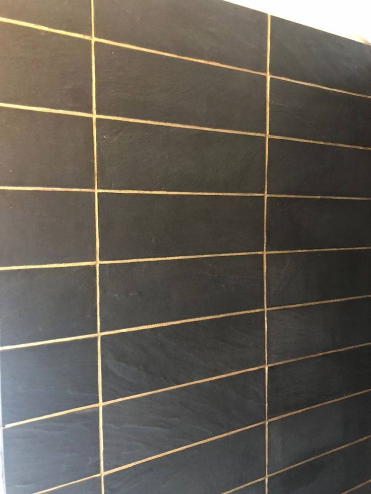 a bathroom with black tile and gold lines on the wall