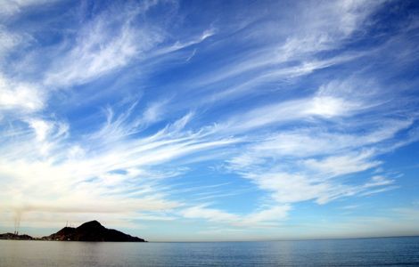 the sky is filled with clouds and some small island in the distance on the water