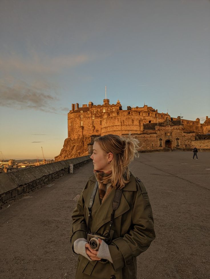 a woman standing in front of an old castle with a camera on her hand and looking off into the distance