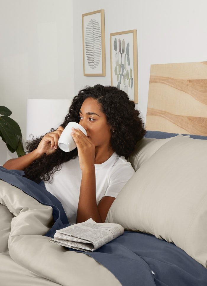 a woman laying in bed drinking from a cup