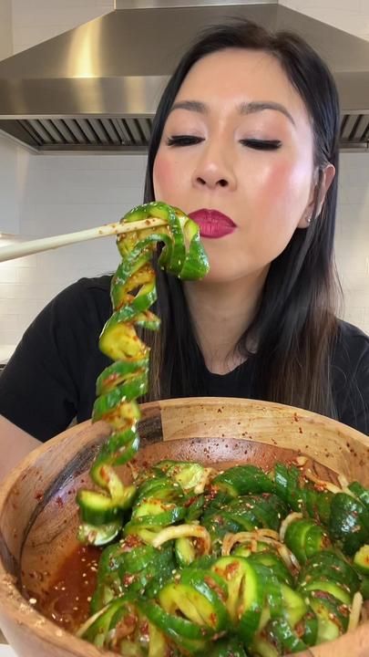 a woman holding chopsticks in her mouth while she eats some food with green peppers