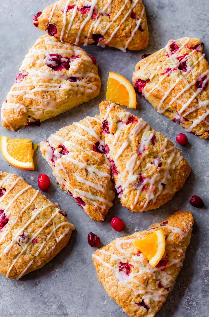 cranberry orange scones with icing on a baking sheet next to sliced oranges and cranberries