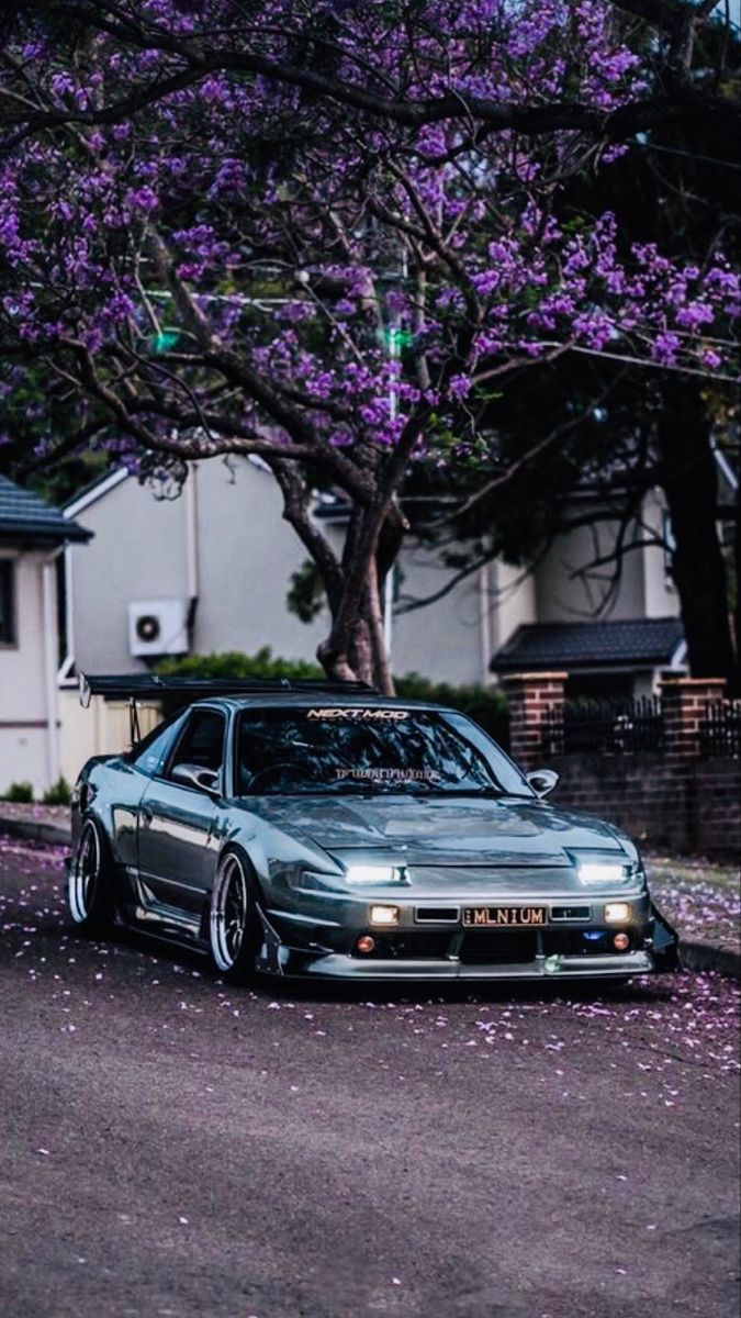 a car parked in front of a tree with purple flowers