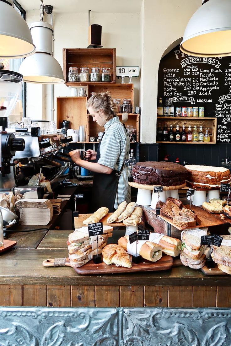 a woman working in a bakery with lots of bread and pastries on the counter