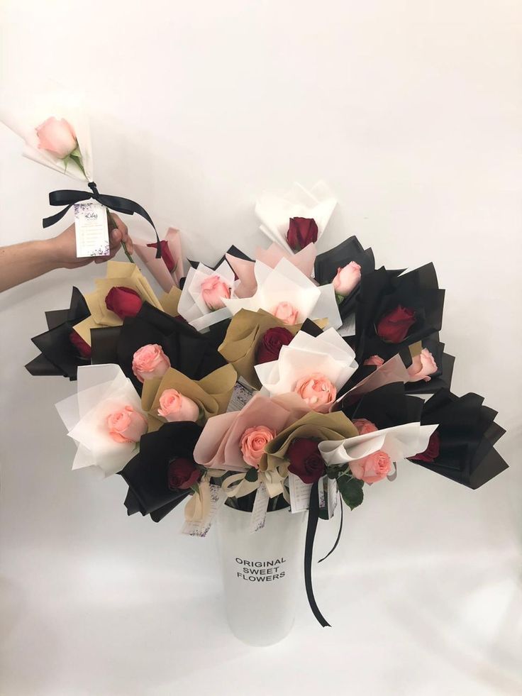 a white vase filled with flowers on top of a white table next to a person's hand