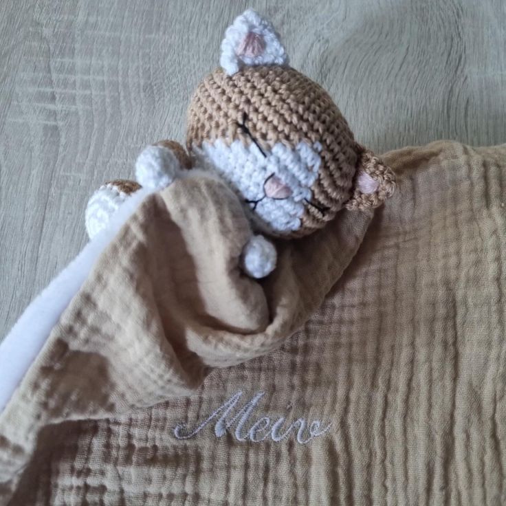 a crocheted cat laying on top of a bed next to a name blanket