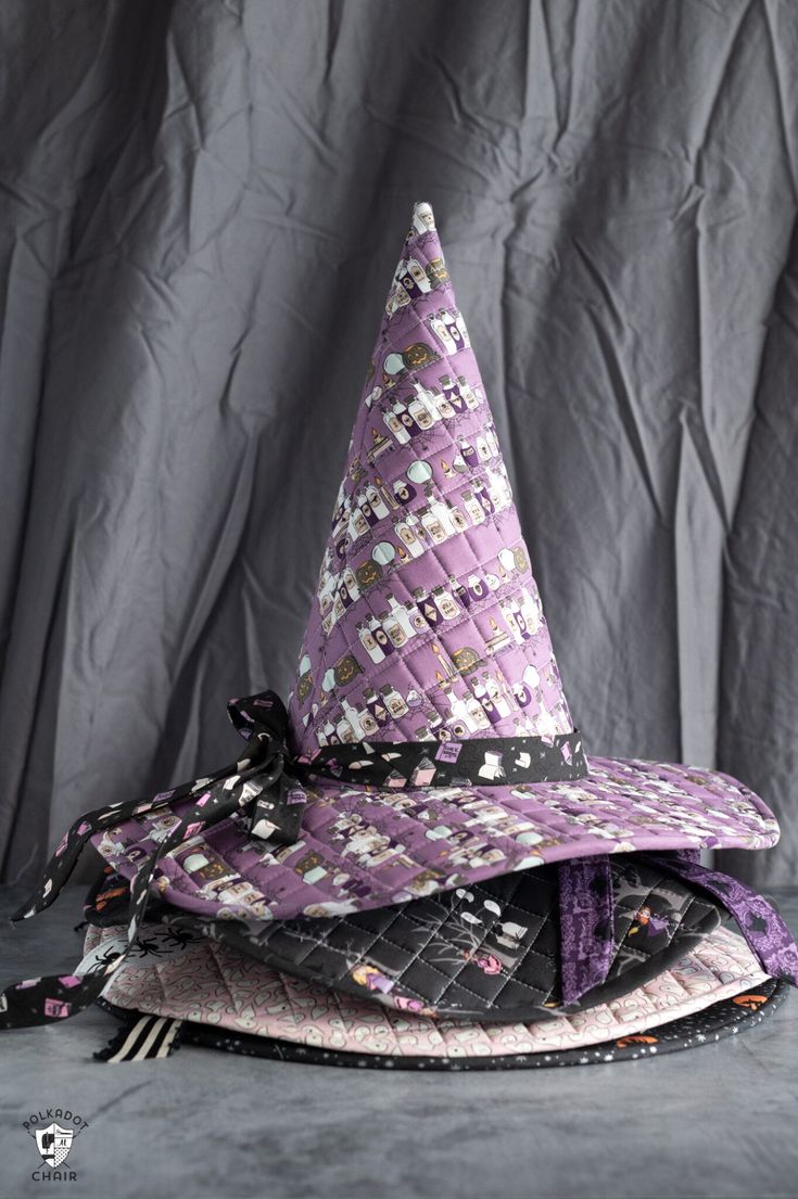 a purple and black hat sitting on top of a pile of cloths next to a gray background