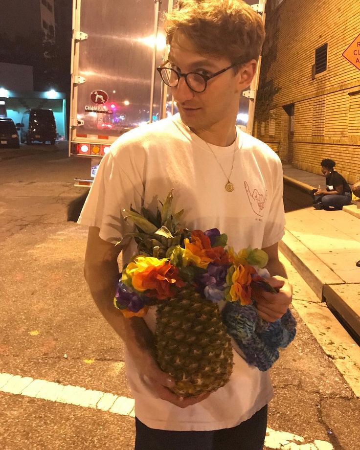 a young man holding a pineapple and flowers in his hands on the side of the road