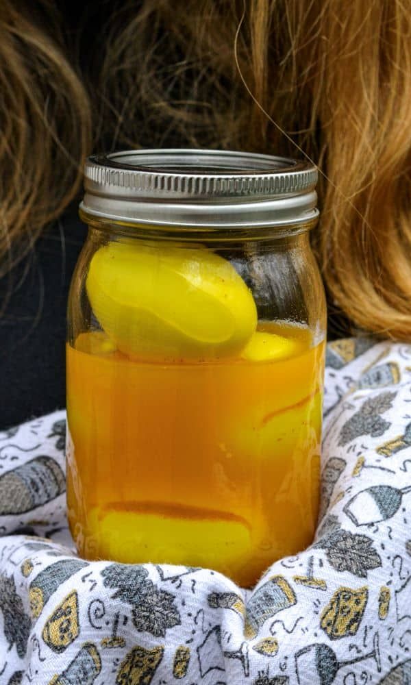 a jar filled with yellow liquid sitting on top of a white and blue cloth next to a woman's head