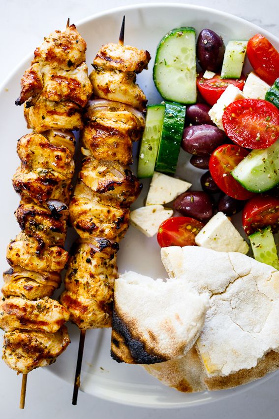 a white plate topped with meat and veggies on skewered skewers