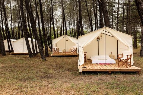 two tents are set up in the woods with tables and chairs on each side of them