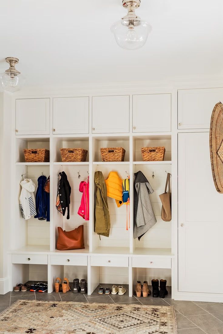 an organized mud room with white cabinets and hanging coats on hooks, shoes and bags