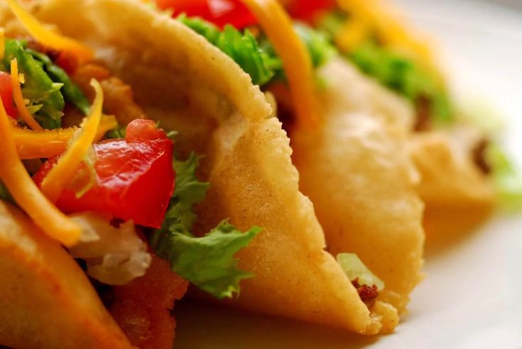 three tacos with various toppings sit on a white plate, ready to be eaten