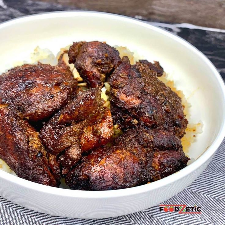 a white bowl filled with meat and rice on top of a checkered table cloth