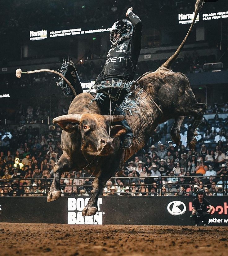 a man riding on the back of a bull in front of an arena full of people