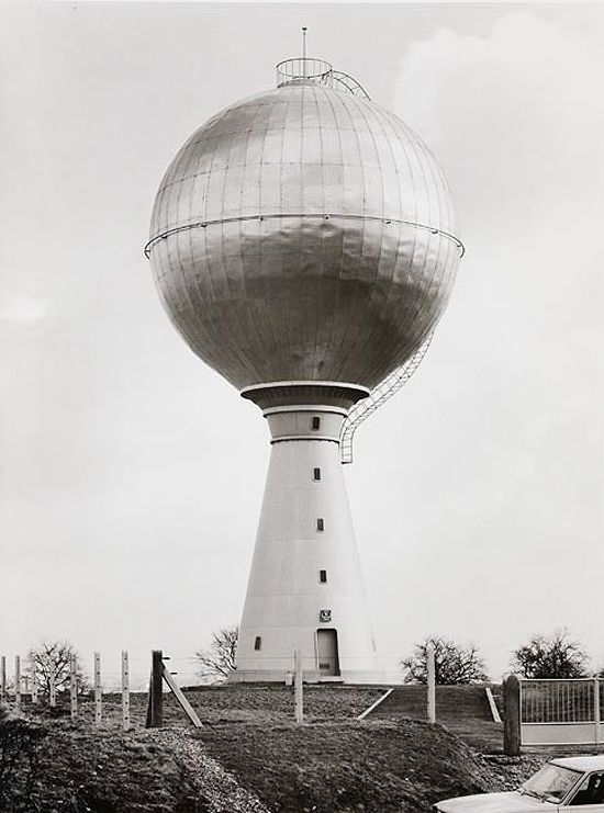 an old photo of a large water tower in the middle of a field with cars parked around it