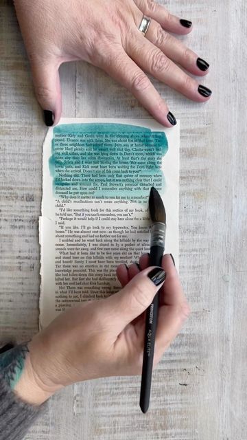 two hands with black nail polish on top of an open book next to a brush