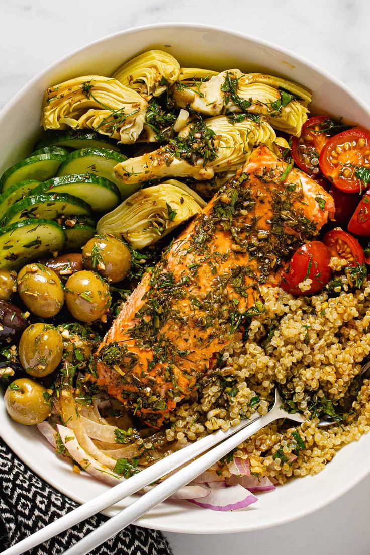 a white bowl filled with salmon, vegetables and couscouse next to chopsticks