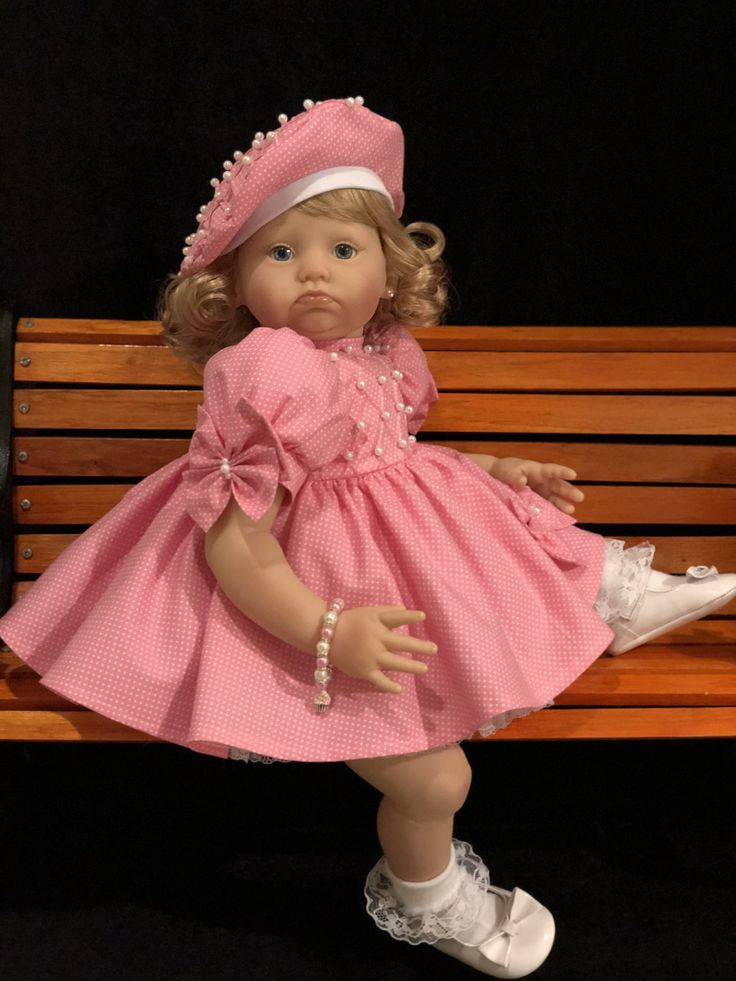 a doll is sitting on a bench wearing a pink dress and white shoes with pearls