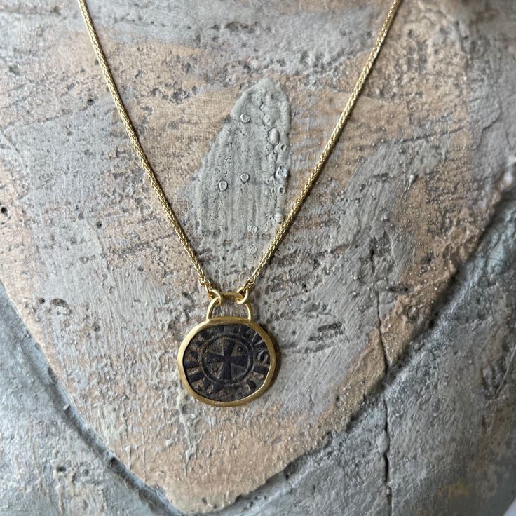 a necklace with a compass on it sitting on top of a piece of rock next to a stone wall