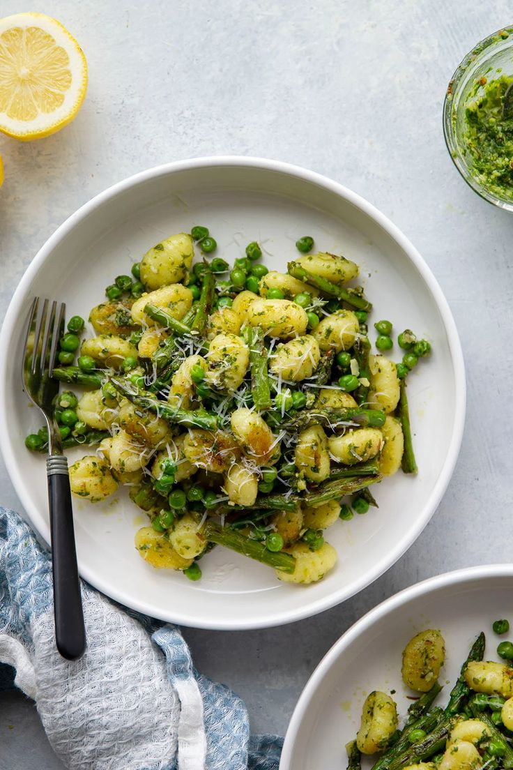 two white plates with pasta and asparagus on them next to lemon wedges