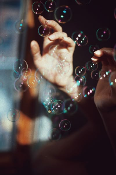 a person holding bubbles in front of their face while looking out the window at something