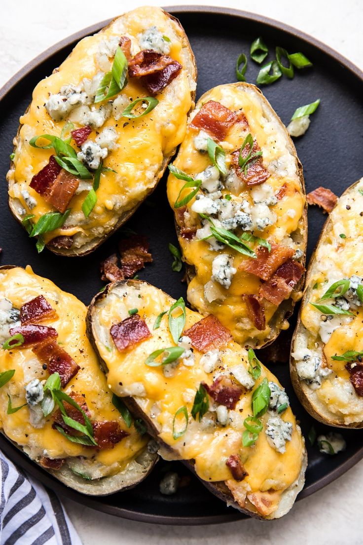 baked potatoes with bacon, cheese and green onions on a black plate next to a striped napkin