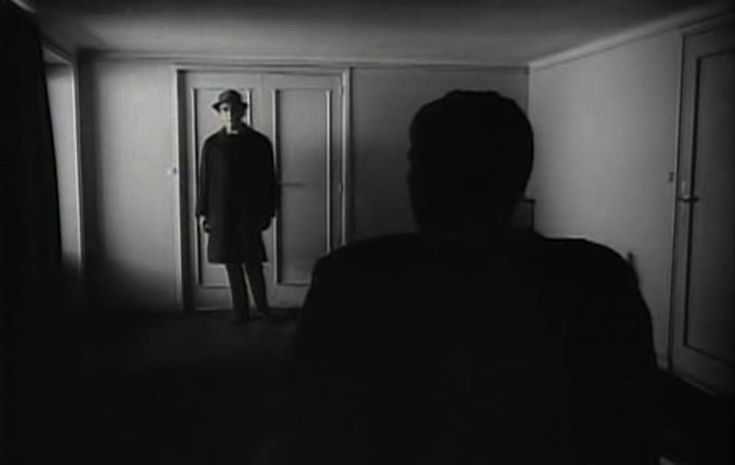 a man standing in front of a doorway with his back turned to the camera, wearing a suit and hat