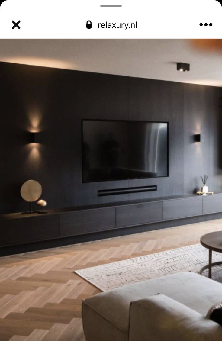 a living room with black walls and wooden flooring is lit by recessed lights