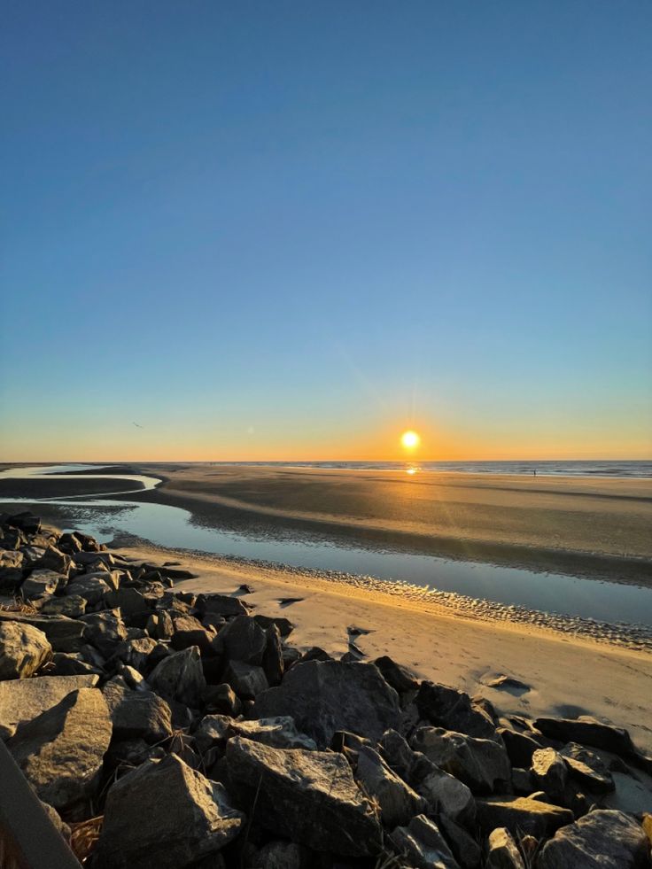 the sun is setting over some rocks on the beach by the water's edge