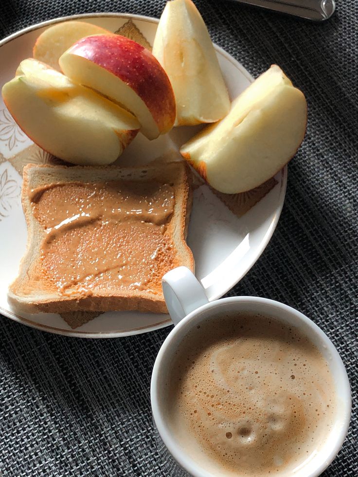 an apple and peanut butter sandwich on a plate next to a cup of coffee