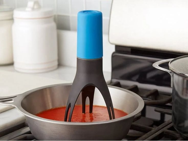 a blue and black spatula is in a silver pan on the stove with red sauce