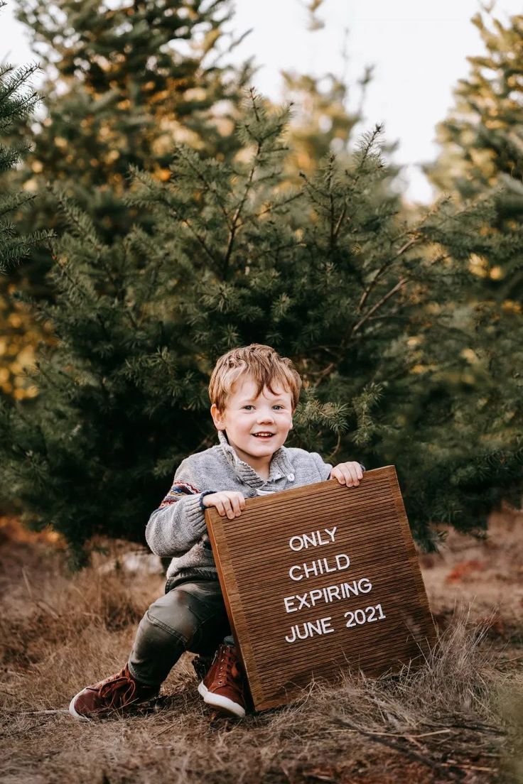 a little boy sitting on the ground holding a sign