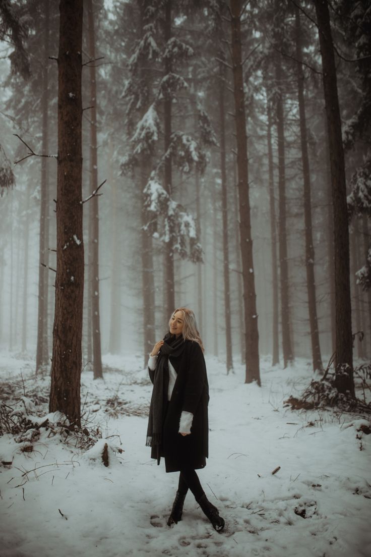 a woman is walking through the woods in the snow, with her eyes closed and she's wearing a black coat