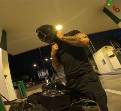 a man in black shirt and helmet on motorcycle at gas station with lights shining from the tank