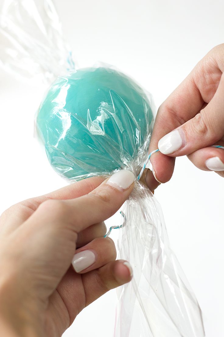 two hands holding a plastic bag filled with blue candies and one hand reaching for the candy