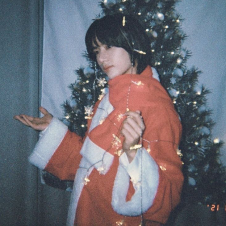 a woman wearing a red and white jacket standing in front of a christmas tree