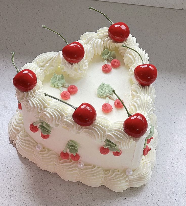 a heart shaped cake with cherries on the top and white frosting, sitting on a table