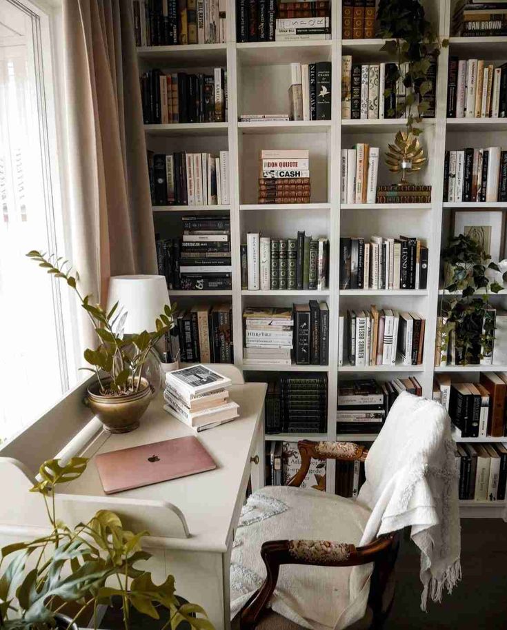 a room filled with lots of books next to a white desk and chair in front of a window