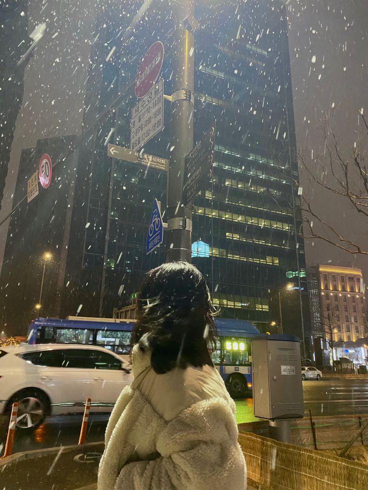 a woman standing in front of a tall building on a city street covered in snow