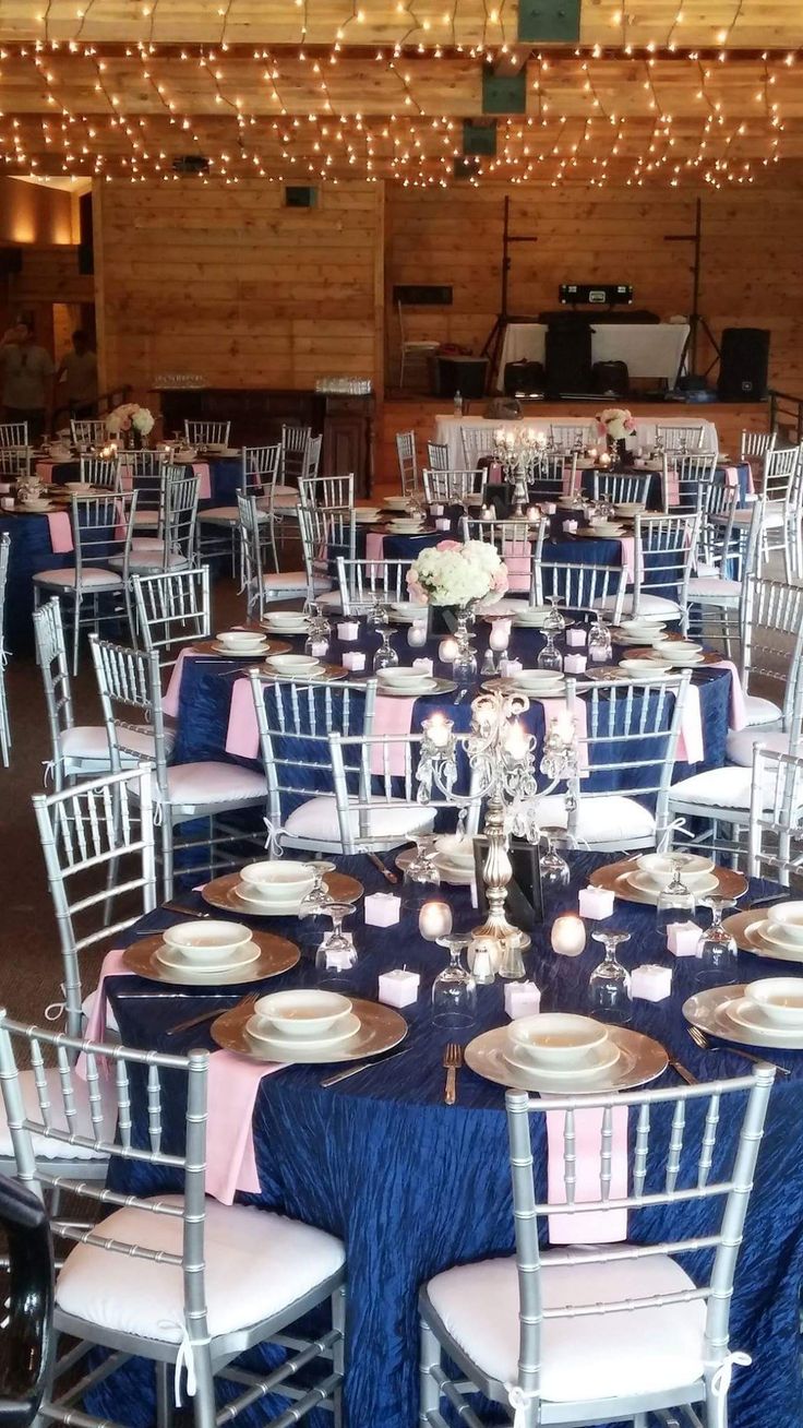 the tables are set with white and blue linens, silverware, and pink napkins