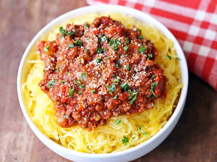 a white bowl filled with spaghetti and sauce on top of a wooden table next to a fork