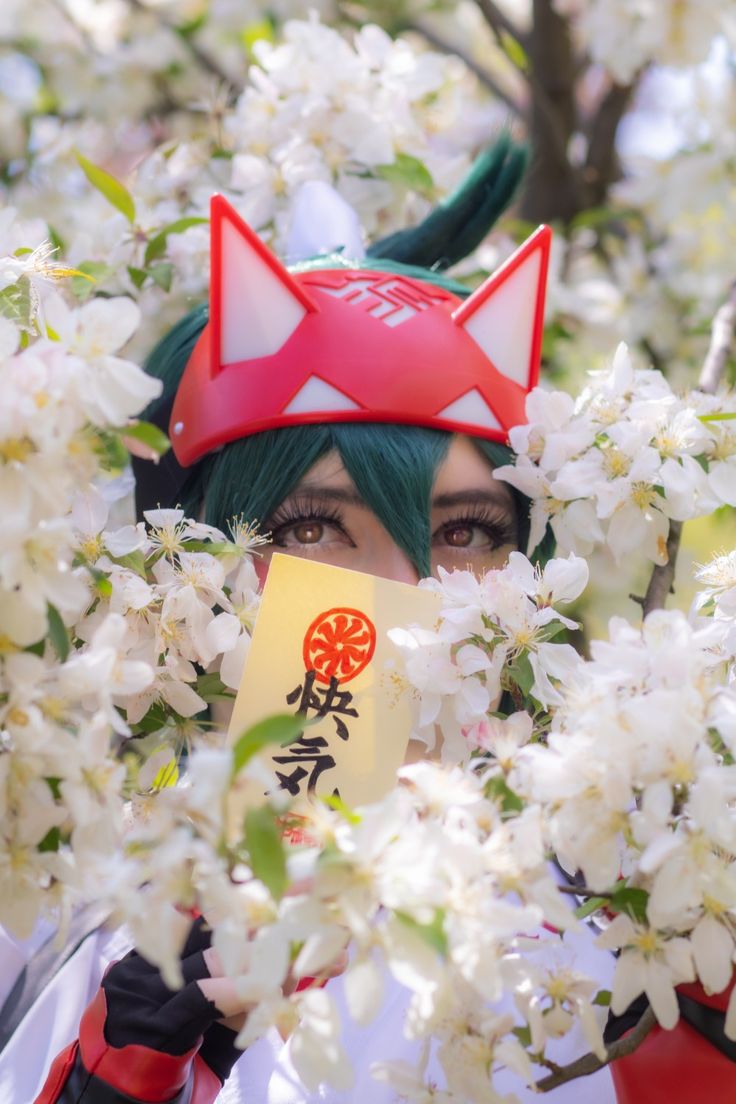 a woman with green hair wearing a red and white cat hat holding a sign in front of her face