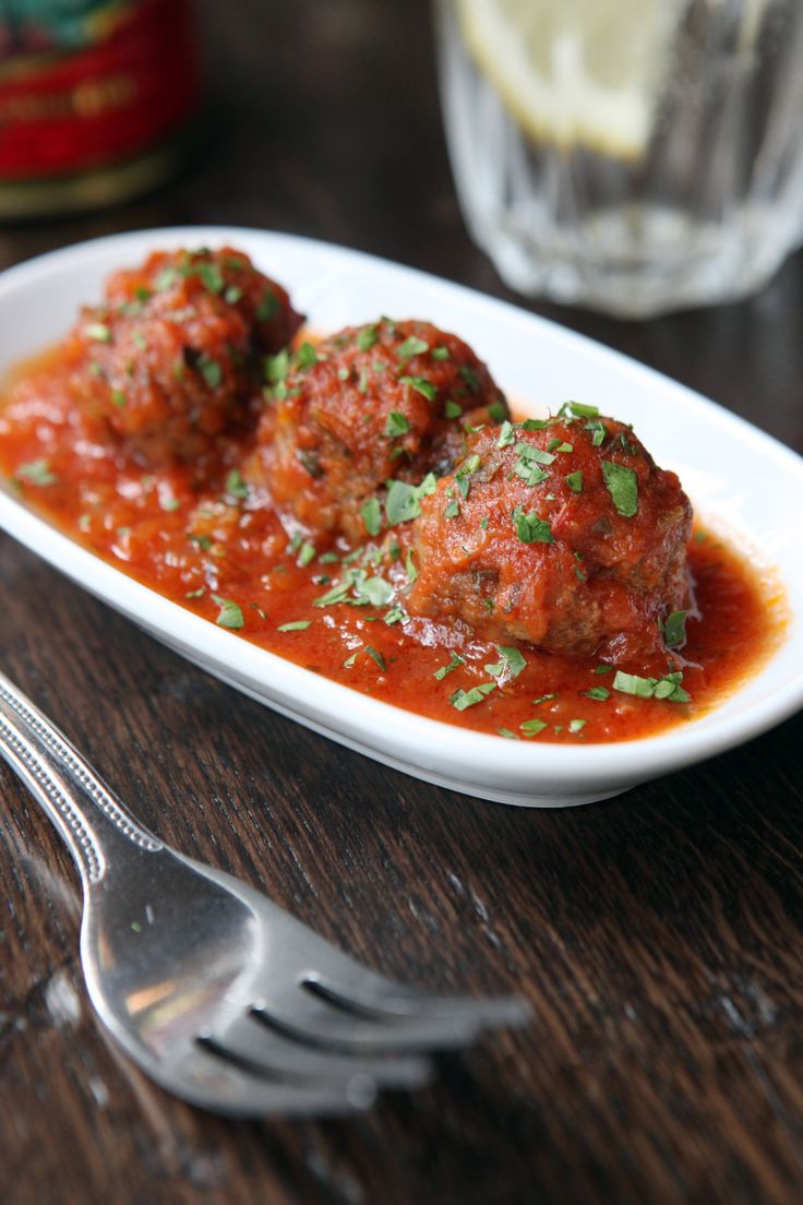 two meatballs covered in marinara sauce on a white plate with a fork next to it