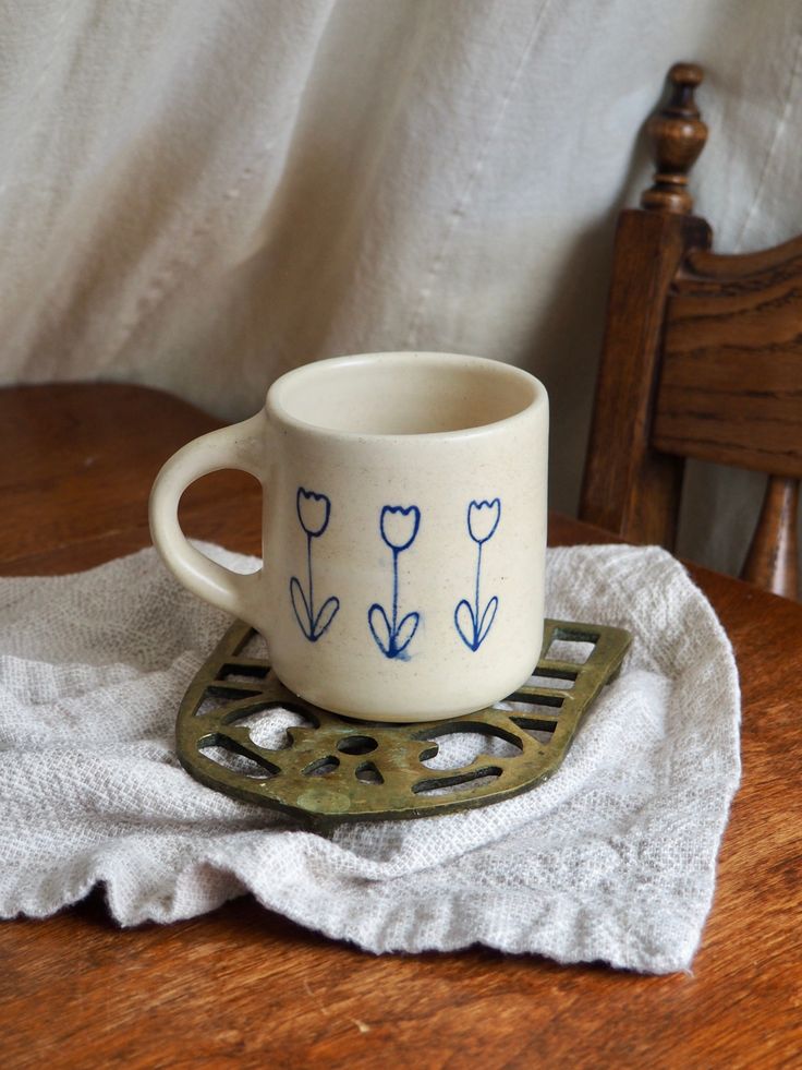 a coffee cup sitting on top of a wooden table next to a white towel and chair