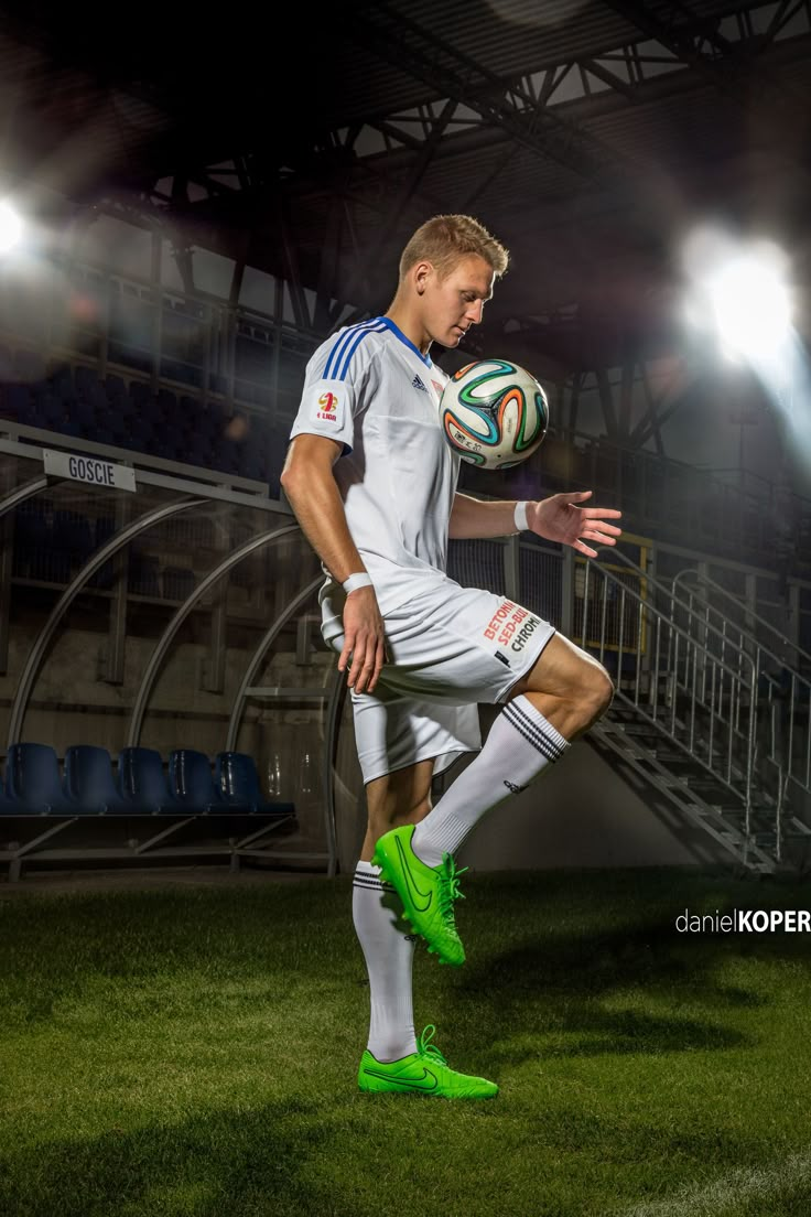 a soccer player in white and green kicks the ball at an indoor stadium with bright lights