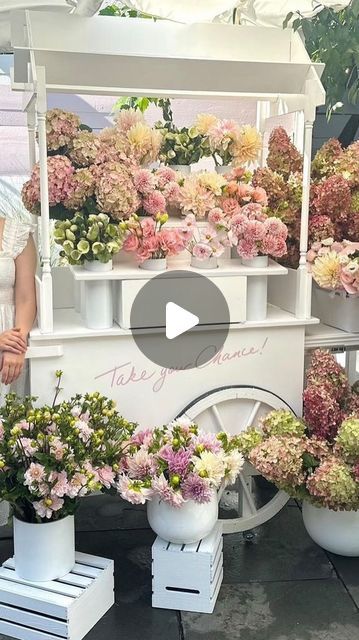 a woman standing next to a white cart filled with flowers