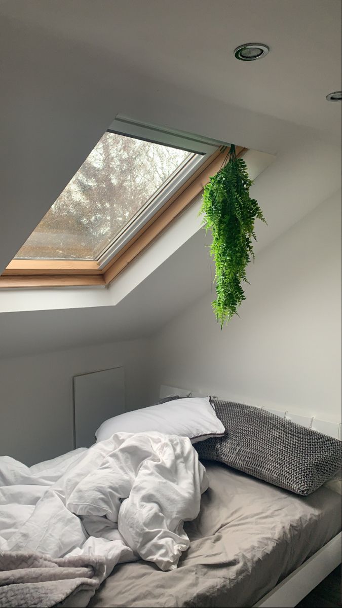 an unmade bed with white sheets and pillows under a skylight